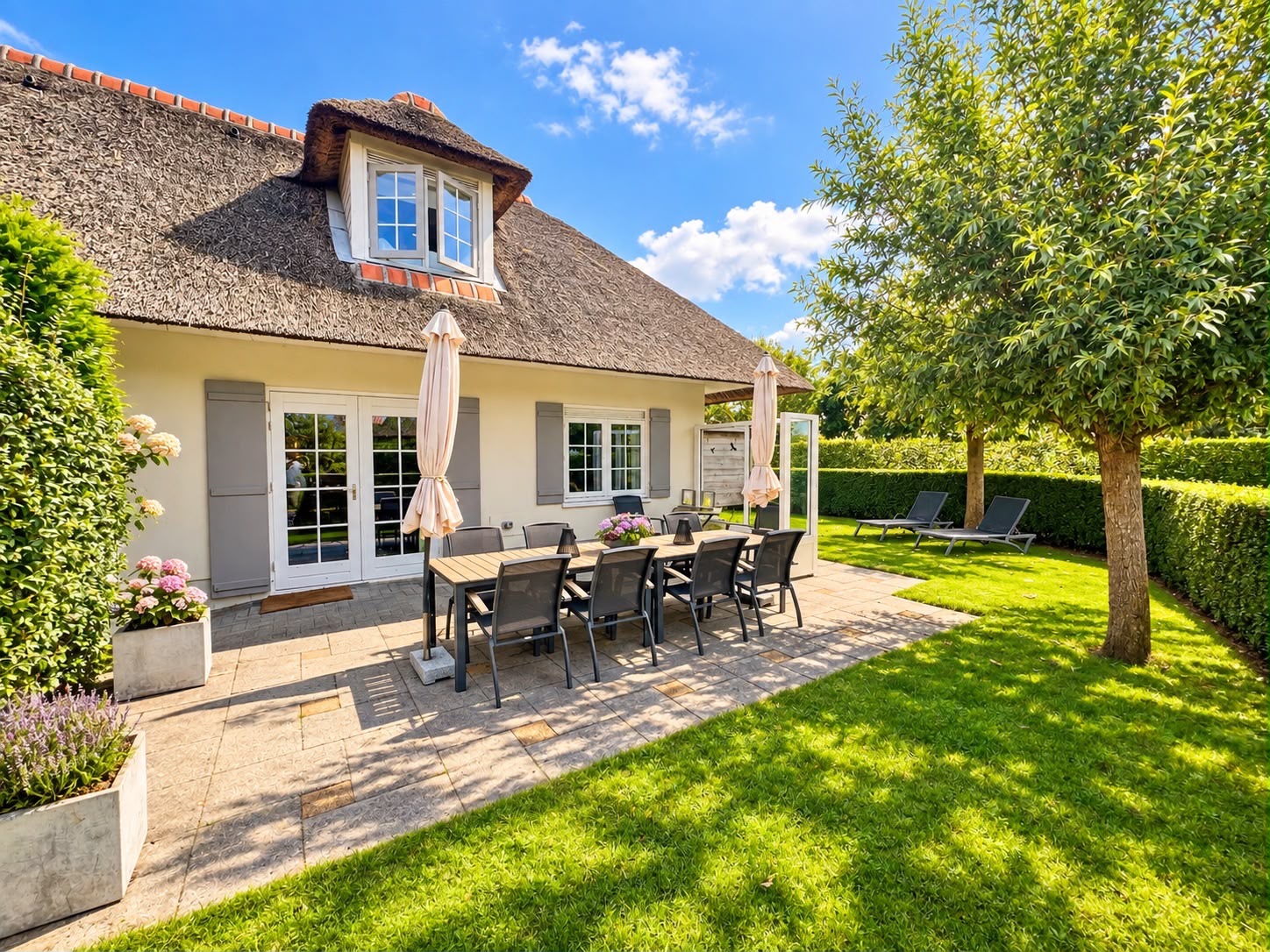 Onze villa met rieten dak, terras met tuintafel en de zonnige tuin met grote boom